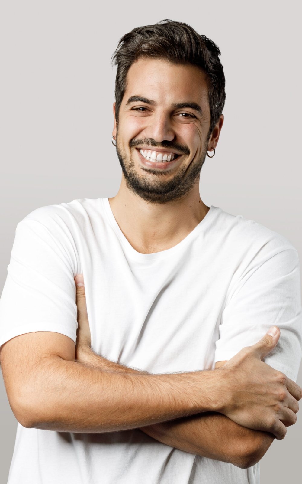 Portrait of handsome smiling man in white t-shirt with crossed arms isolated on gray background.
