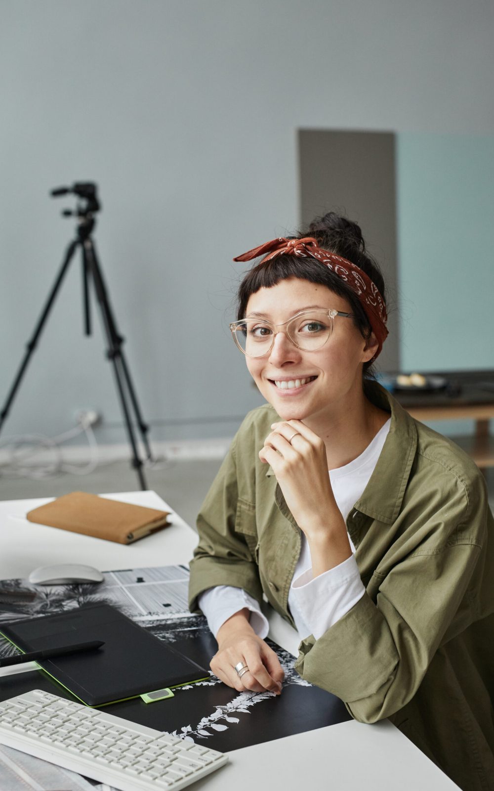Vertical portrait of young female photographer looking at camera while sitting at workplace in photo studio
